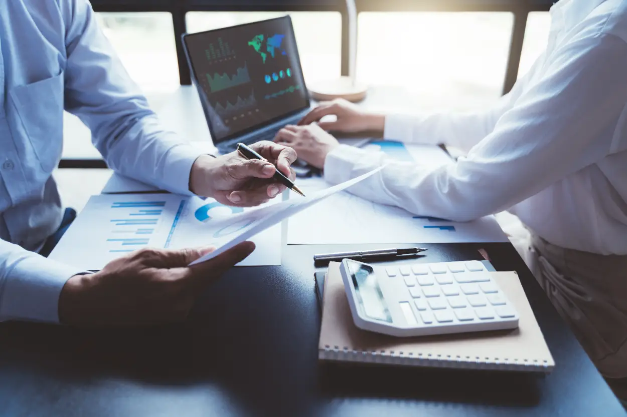 Raporlar, hesap makinesi ve dizüstü bilgisayardaki finansal tablolar üzerinden bütçe planlaması yapan iki iş insanı